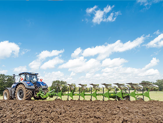 new holland traktor zieht amazone pflug über feld blauer himmel wolken